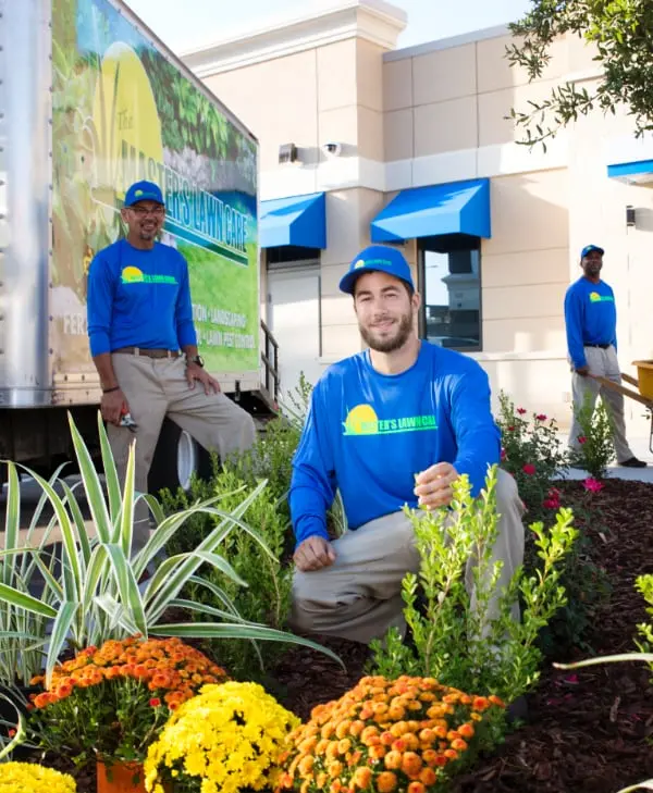 Team member kneeling and smiling within a bed of flowers